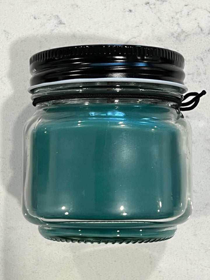 Side view of Seven Seas scented candle in 8 oz mason jar with wood wick, soy-paraffin wax, and a bold fragrance blend of teakwood, leather, tobacco, and sea salt